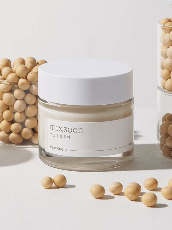 K-beauty fermented bean cream in a glass jar surrounded by soybeans on a light background.